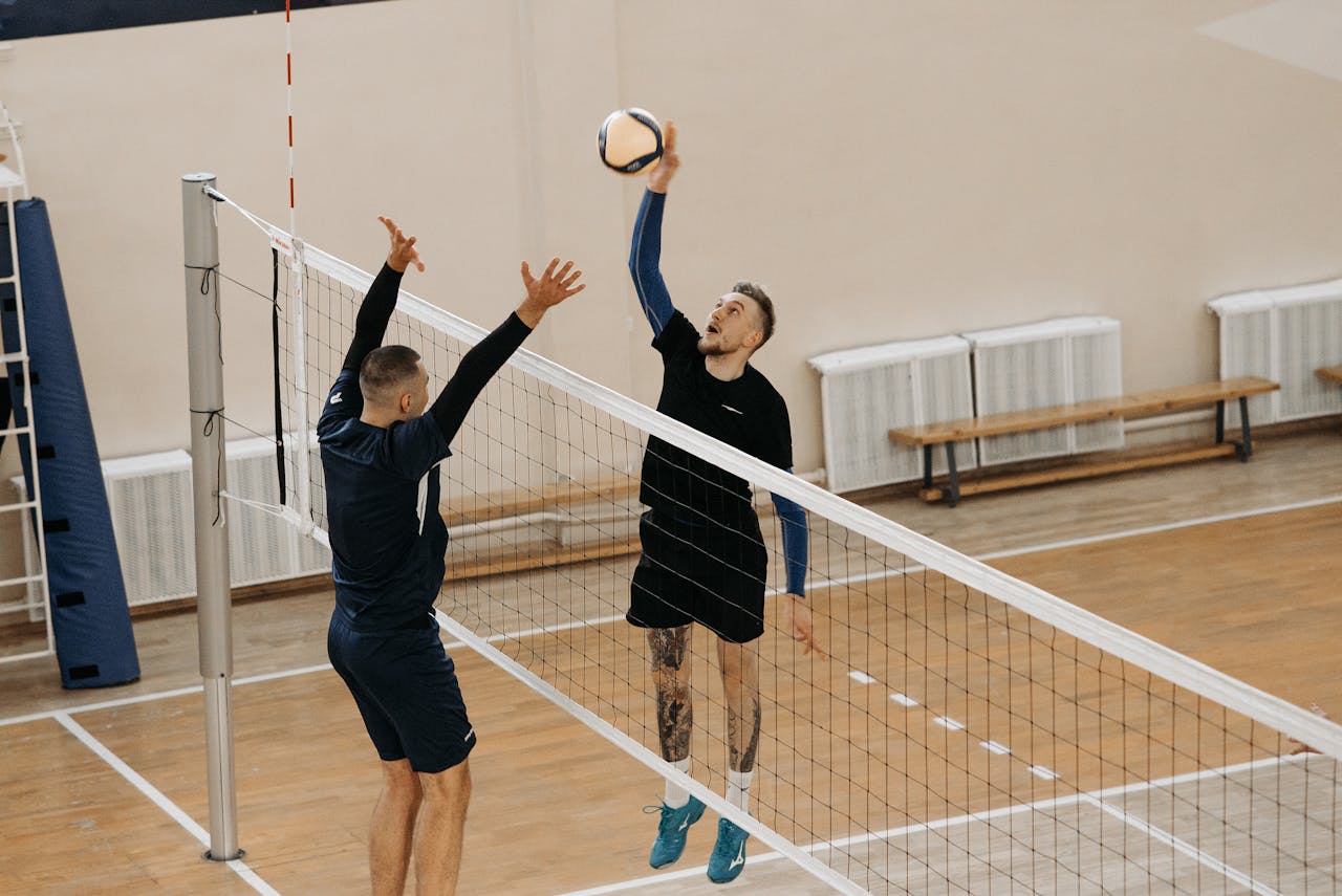 Two male athletes playing a competitive volleyball game indoors.