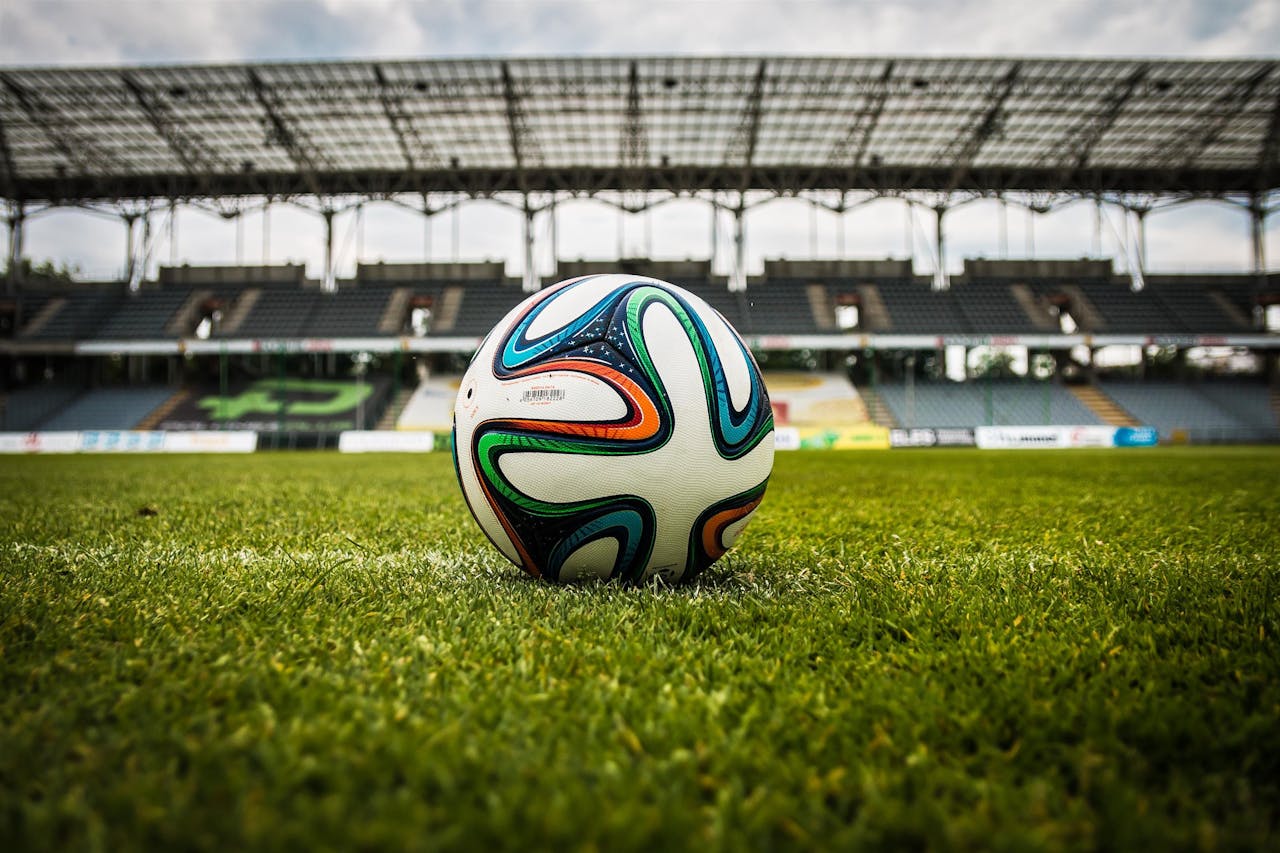 hero-img A vibrant soccer ball rests on a lush green field inside an empty stadium, capturing the essence of sports.