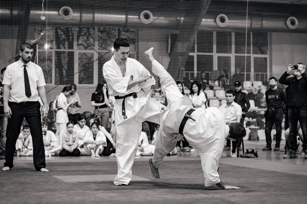 Black and white action shot of a karate match at a tournament, showcasing skillful combat.