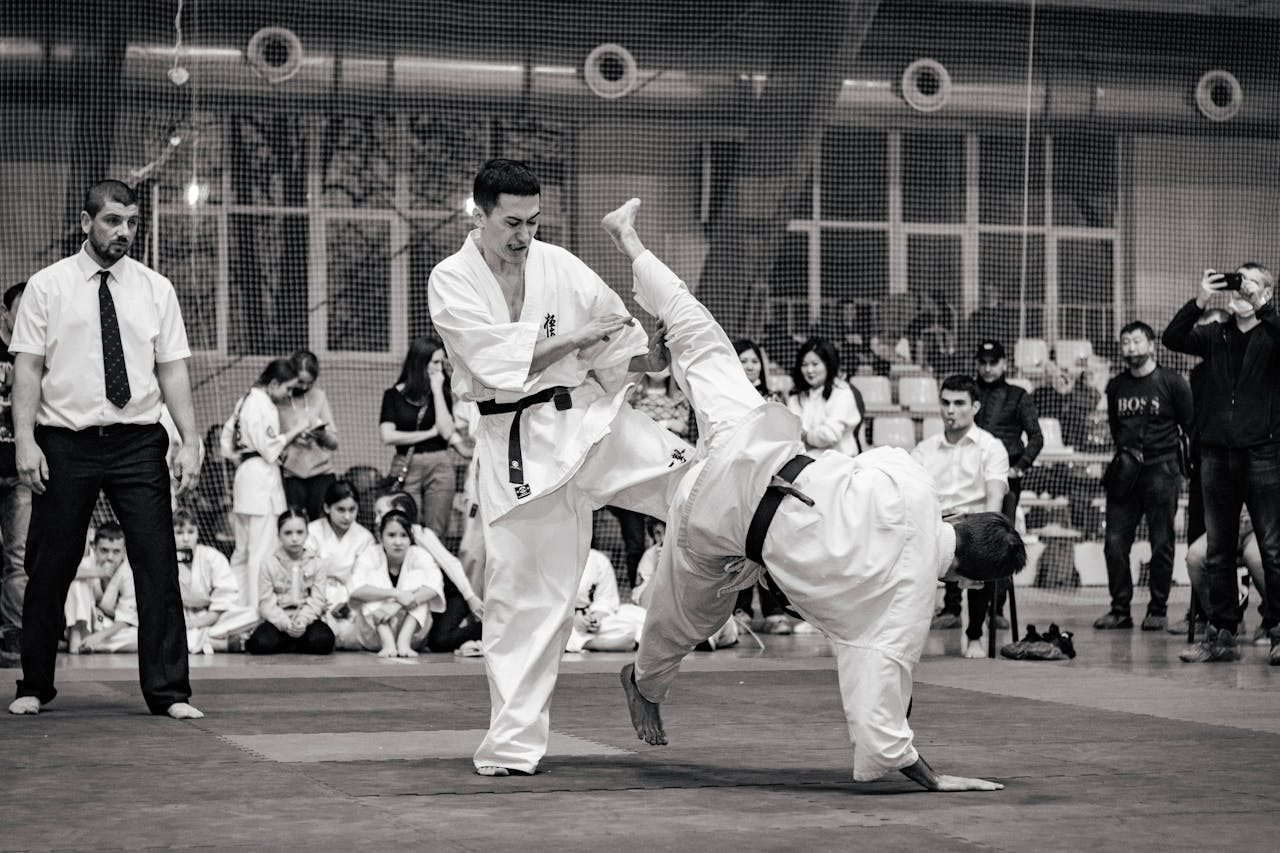 Black and white action shot of a karate match at a tournament, showcasing skillful combat.