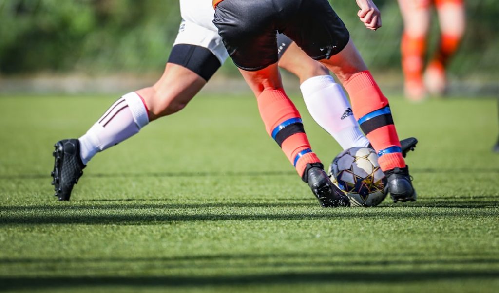 woman-in-black-and-white-soccer-jersey-kicking-soccer-ball-on-green-field-during-daytime-5ynjx9no3yc